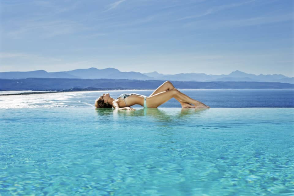 girl posing in an infinity pool on the garden route with mountains in the distance