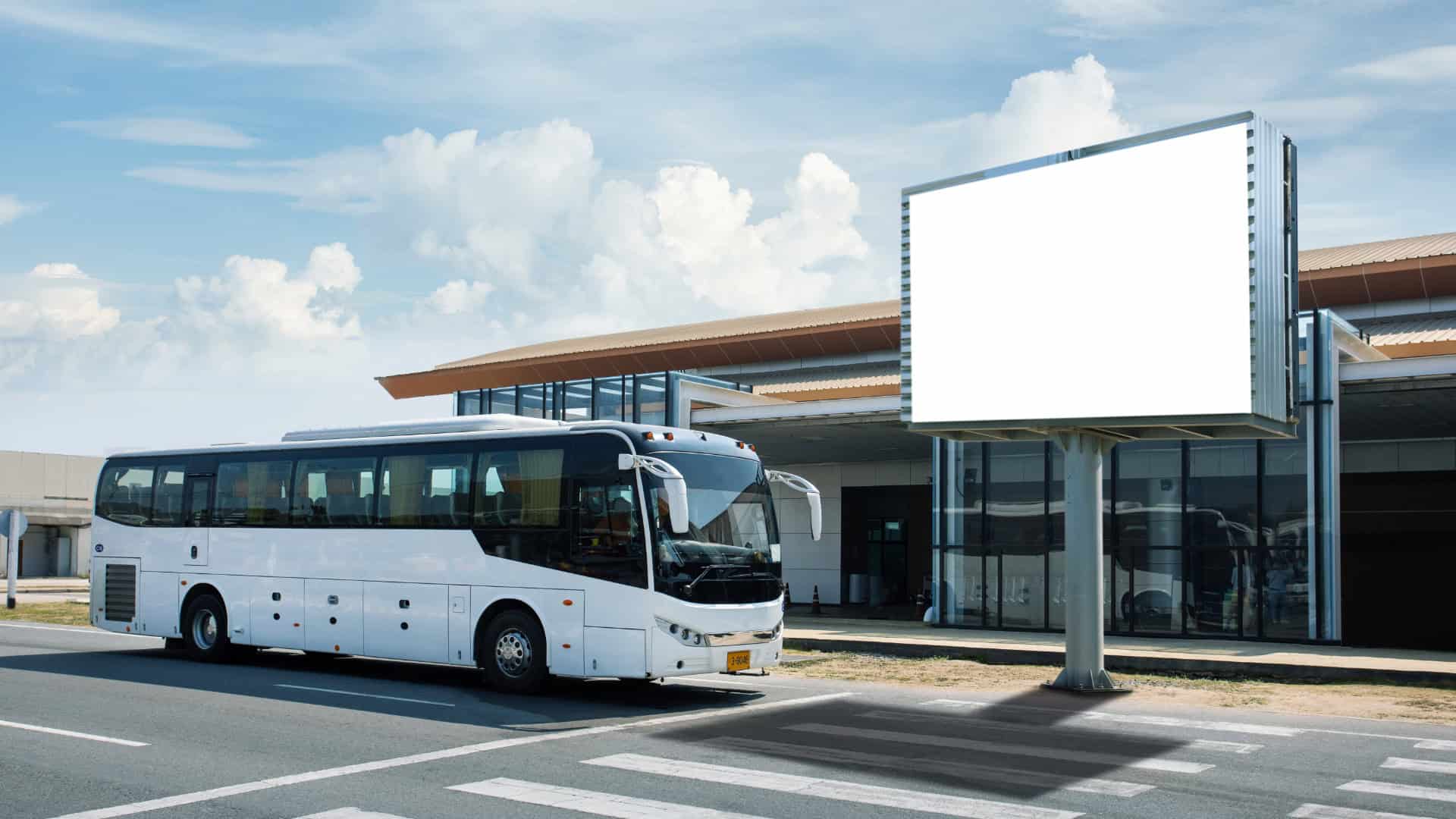 shuttle bus parked in front of airport terminal alongside large outdoor advertising signage